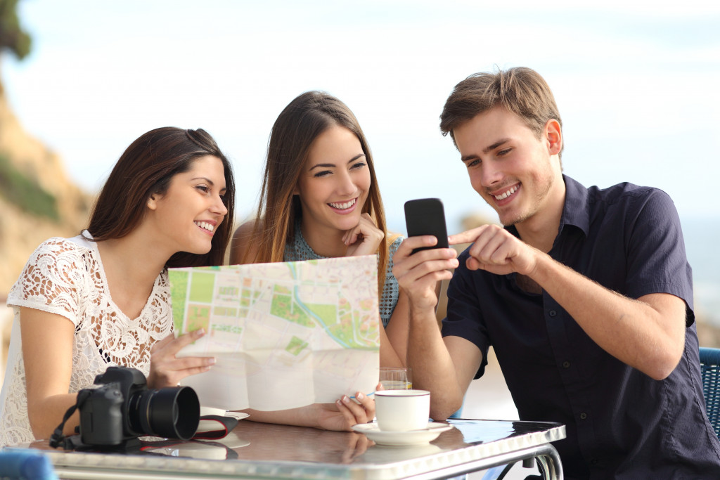 Group of young tourist friends consulting gps map in a smart phone in a restaurant with the beach in the background